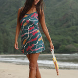 woman with dark brown hair wearing mini spaghetti strap dress in dark teal with shell and lei print