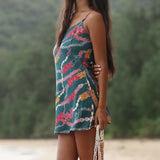 woman with dark brown hair wearing mini spaghetti strap dress in dark teal with shell and lei print