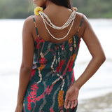 woman with dark brown hair wearing mini spaghetti strap dress in dark teal with shell and lei print