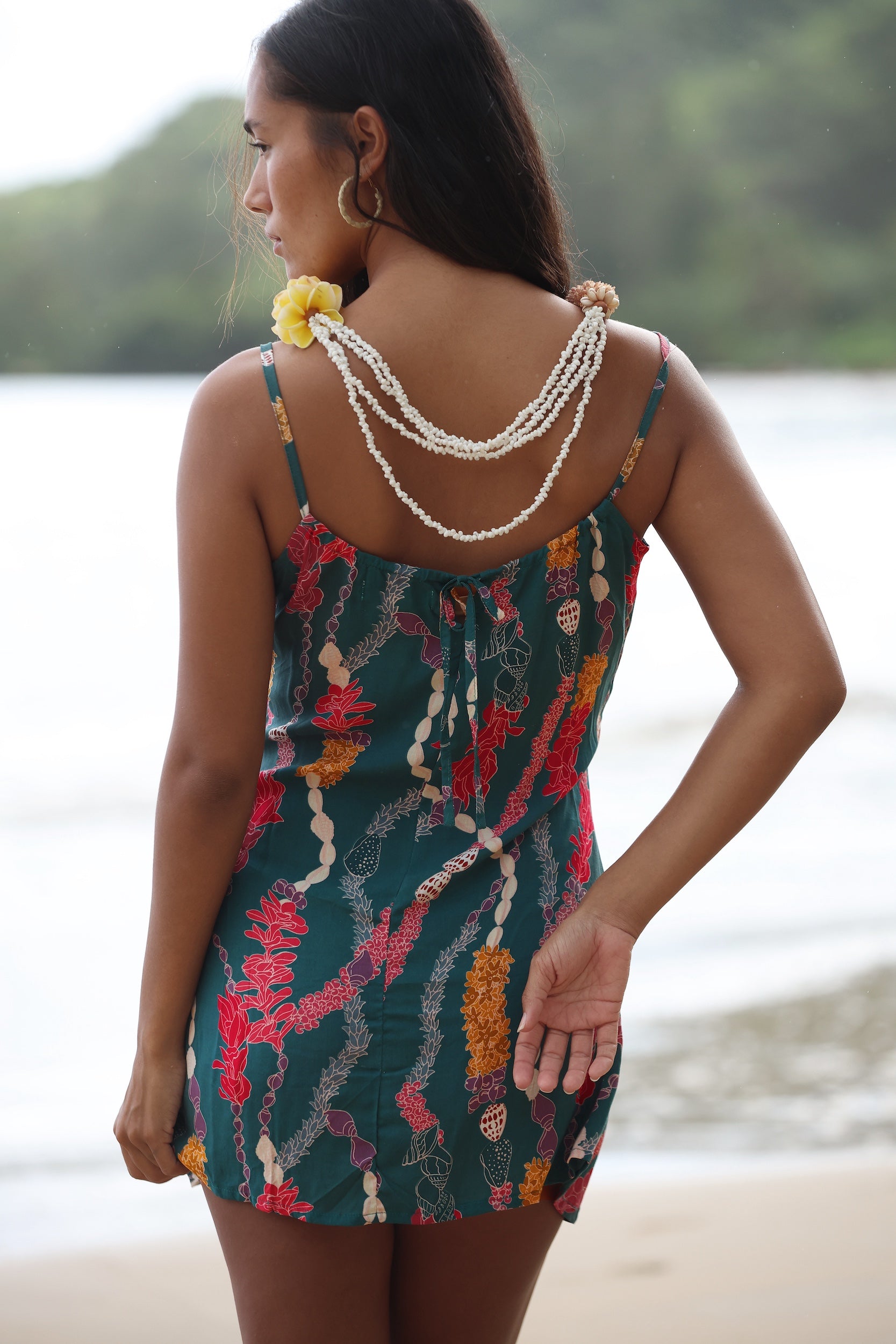 woman with dark brown hair wearing mini spaghetti strap dress in dark teal with shell and lei print