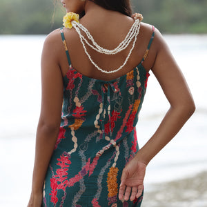 woman with dark brown hair wearing mini spaghetti strap dress in dark teal with shell and lei print