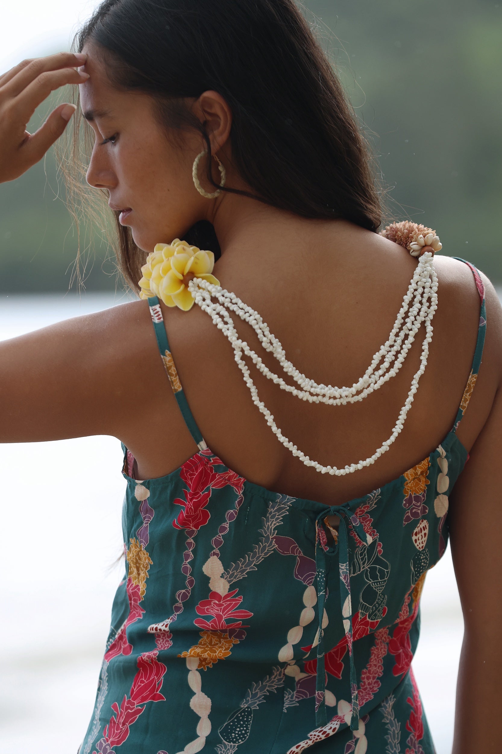 woman with dark brown hair wearing mini spaghetti strap dress in dark teal with shell and lei print