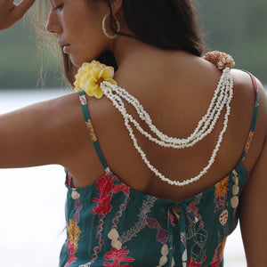 woman with dark brown hair wearing mini spaghetti strap dress in dark teal with shell and lei print