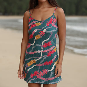 woman with dark brown hair wearing mini spaghetti strap dress in dark teal with shell and lei print