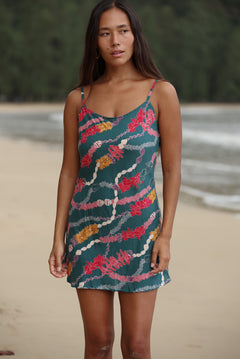 woman with dark brown hair wearing mini spaghetti strap dress in dark teal with shell and lei print