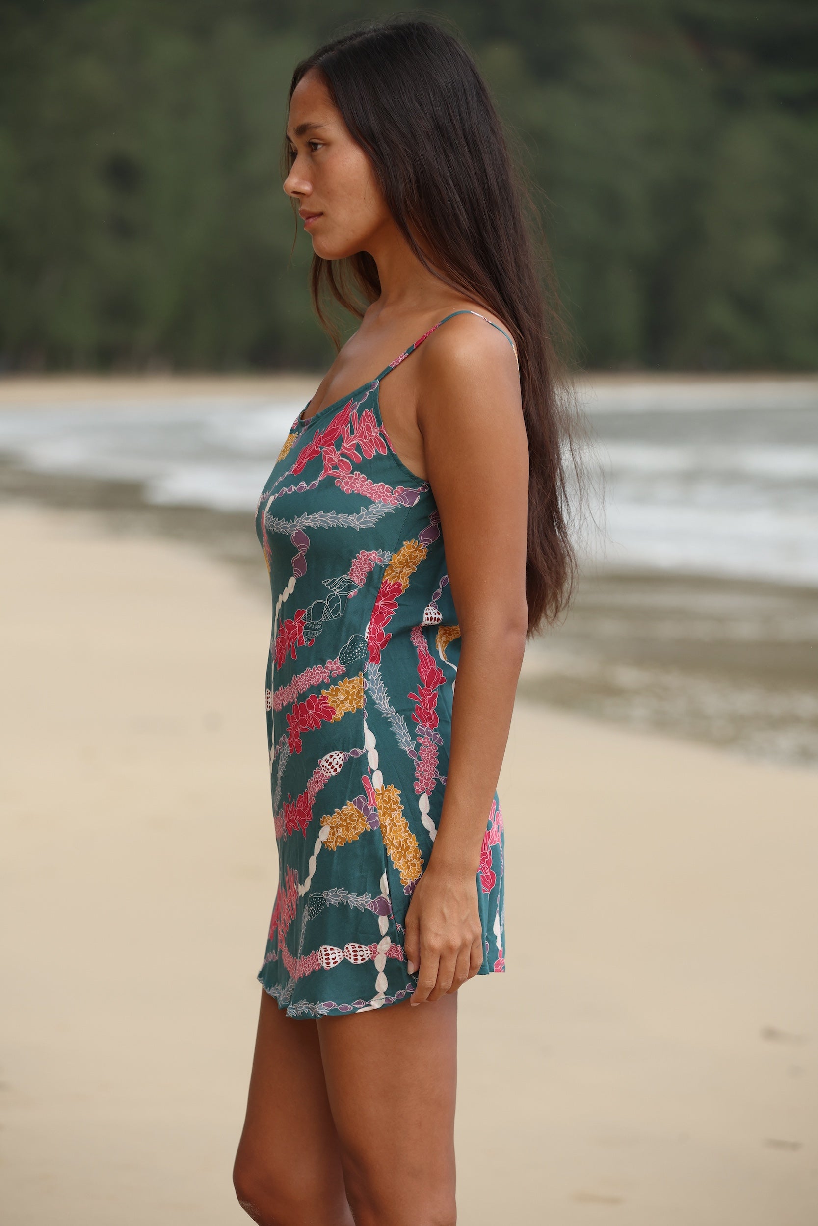 woman with dark brown hair wearing mini spaghetti strap dress in dark teal with shell and lei print