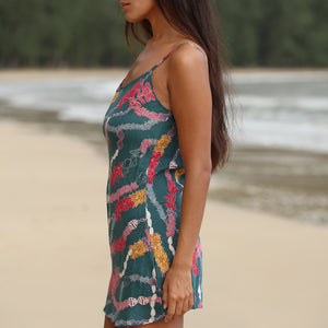woman with dark brown hair wearing mini spaghetti strap dress in dark teal with shell and lei print