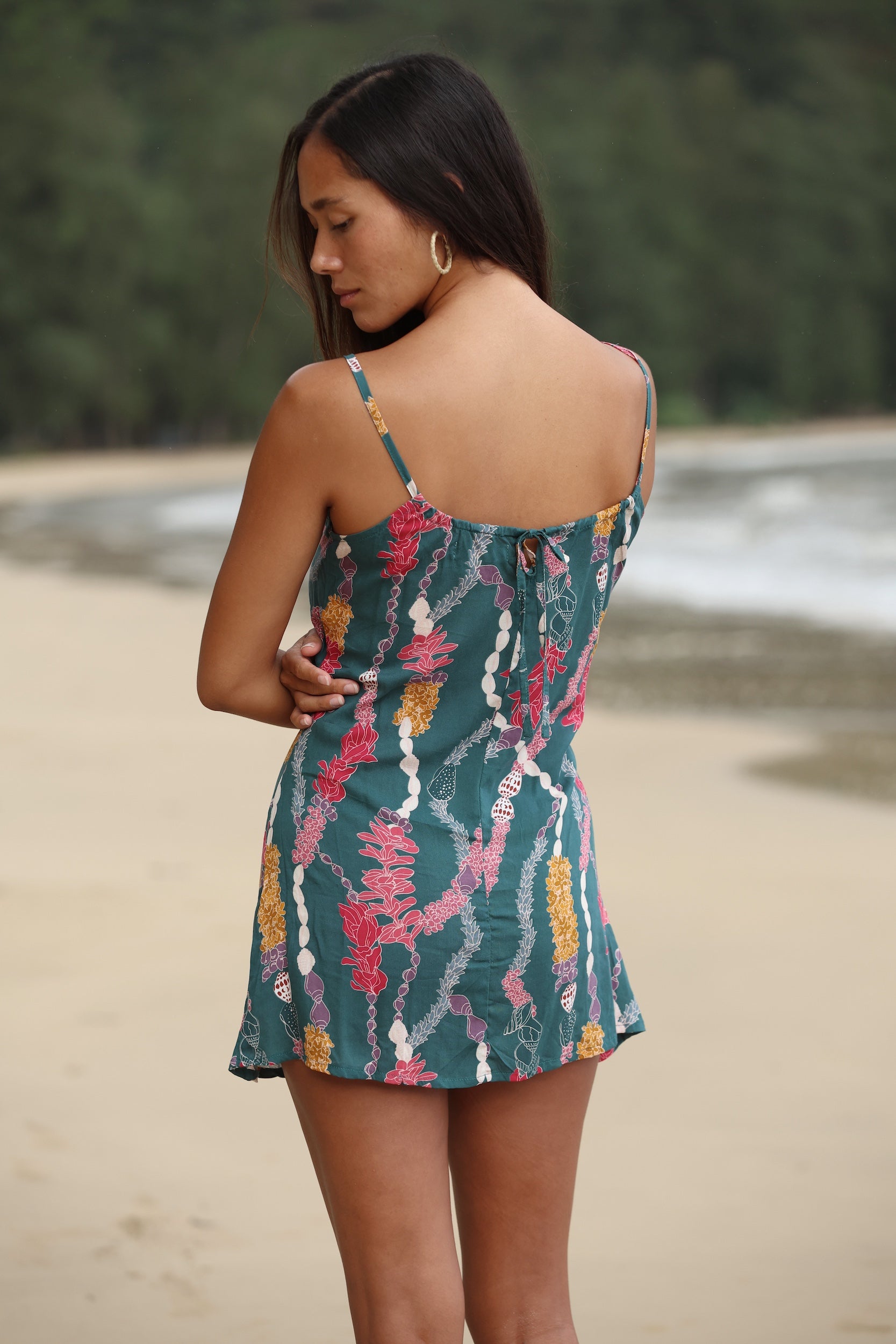 woman with dark brown hair wearing mini spaghetti strap dress in dark teal with shell and lei print