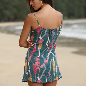 woman with dark brown hair wearing mini spaghetti strap dress in dark teal with shell and lei print