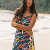 woman with dark brown hair wearing mini spaghetti strap dress in dark teal with shell and lei print