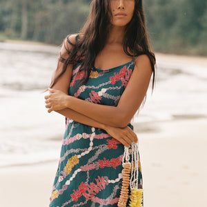woman with dark brown hair wearing mini spaghetti strap dress in dark teal with shell and lei print