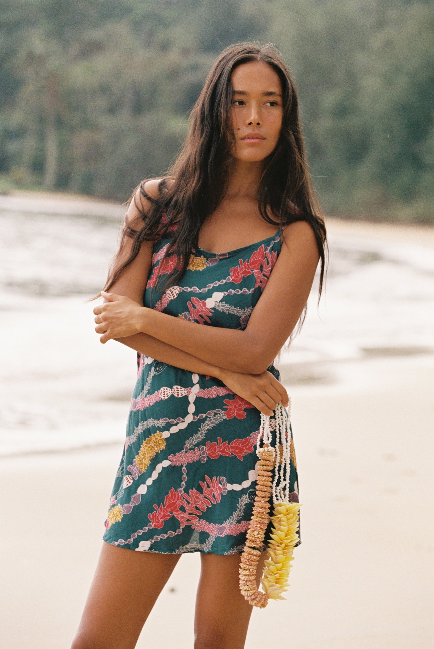 woman with dark brown hair wearing mini spaghetti strap dress in dark teal with shell and lei print