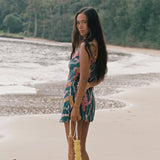 woman with dark brown hair wearing mini spaghetti strap dress in dark teal with shell and lei print