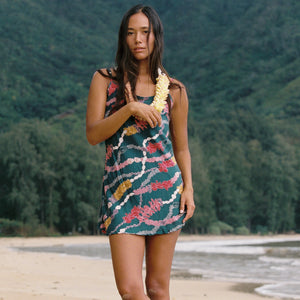 woman with dark brown hair wearing mini spaghetti strap dress in dark teal with shell and lei print