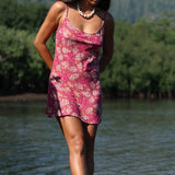 woman with brown hair wearing a pink spaghetti strap scoop neck mini dress with tie back detail in a shell and pua print 