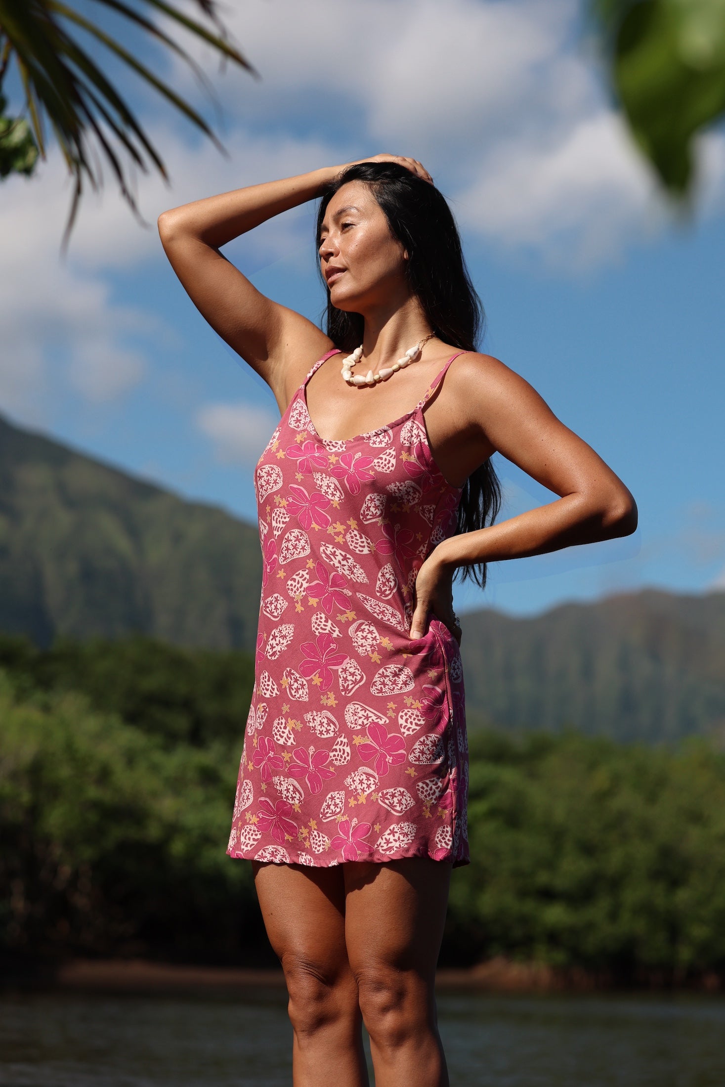 woman with brown hair wearing a pink spaghetti strap scoop neck mini dress with tie back detail in a shell and pua print 