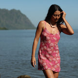 woman with brown hair wearing a pink spaghetti strap scoop neck mini dress with tie back detail in a shell and pua print 