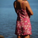 woman with brown hair wearing a pink spaghetti strap scoop neck mini dress with tie back detail in a shell and pua print 