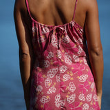 woman with brown hair wearing a pink spaghetti strap scoop neck mini dress with tie back detail in a shell and pua print 