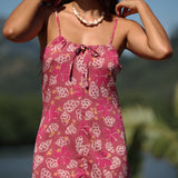 woman with brown hair wearing a pink spaghetti strap scoop neck mini dress with tie back detail in a shell and pua print 