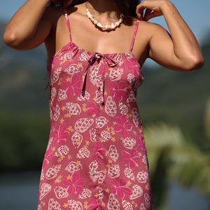 woman with brown hair wearing a pink spaghetti strap scoop neck mini dress with tie back detail in a shell and pua print 