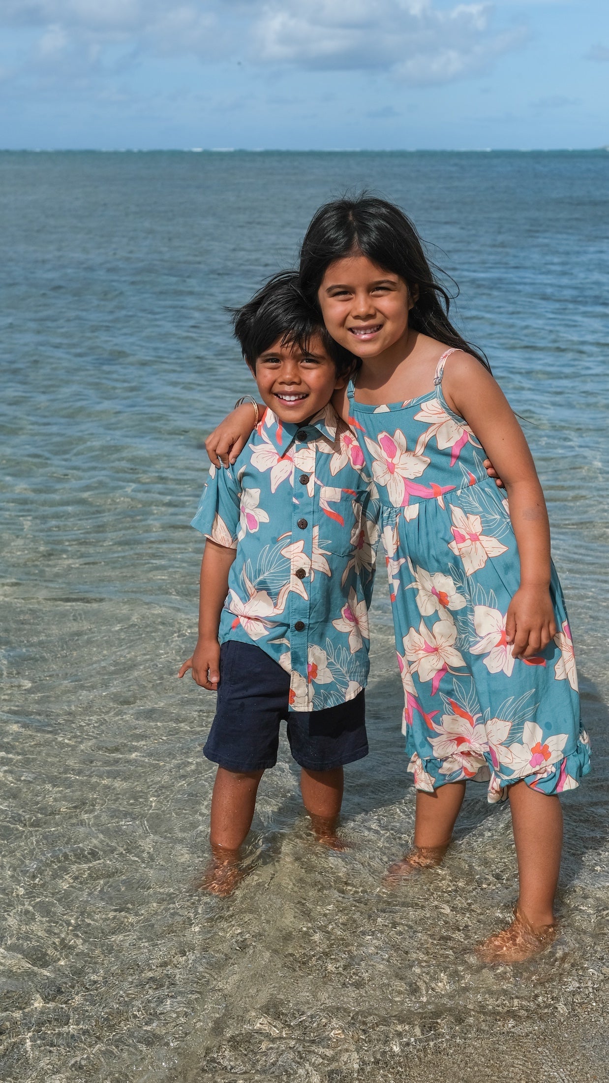 little boy wearing a teal aloha shirt with cream colored orchid blossom pattern