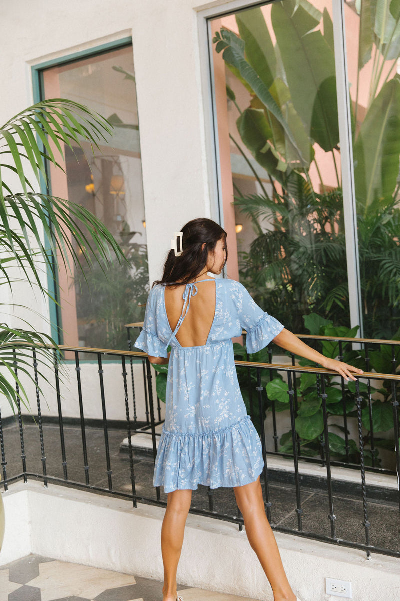 The Yireh Ariana Dress in sky. Romantic and feminine silhouette. This is a versatile style featuring an elastic waist, ruffle hem and flutter sleeves. Open back with a tie around the shoulders. Ethically and sustainably made featuring a one of a kind and exclusive print.