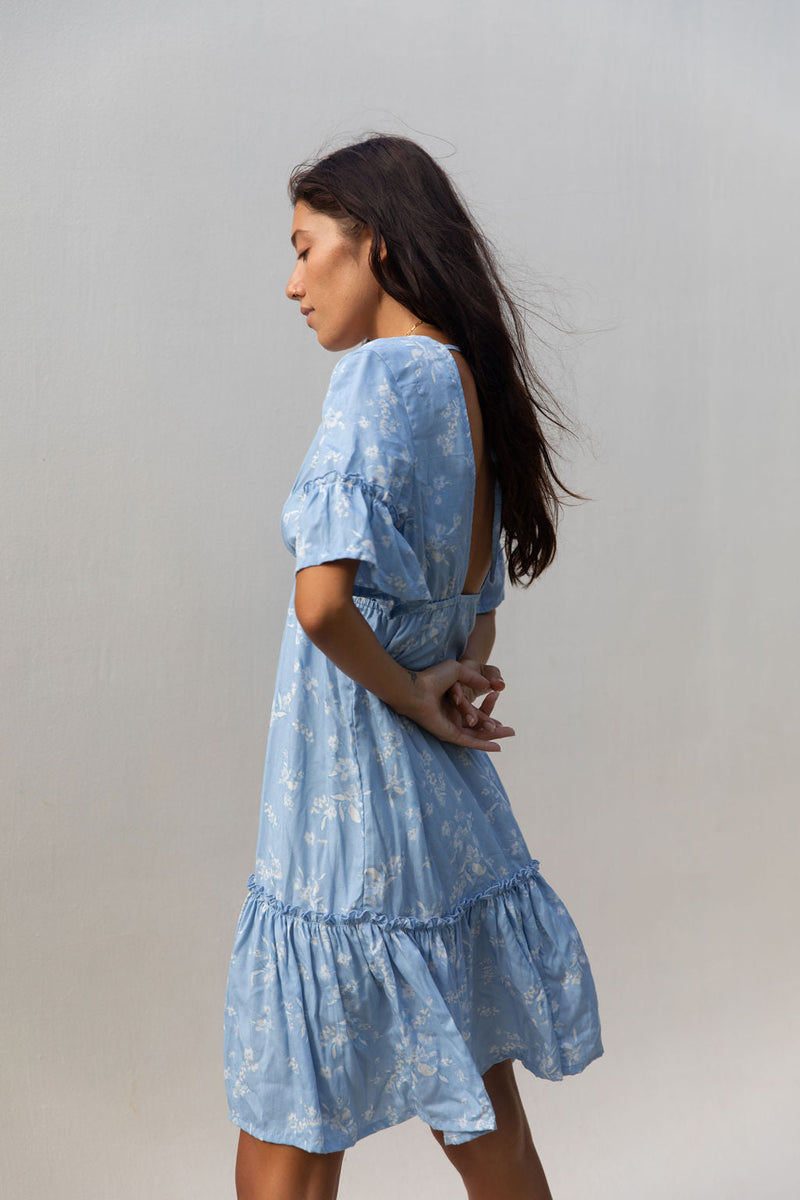 The Yireh Ariana Dress in sky. Romantic and feminine silhouette. This is a versatile style featuring an elastic waist, ruffle hem and flutter sleeves. Open back with a tie around the shoulders. Ethically and sustainably made featuring a one of a kind and exclusive print.
