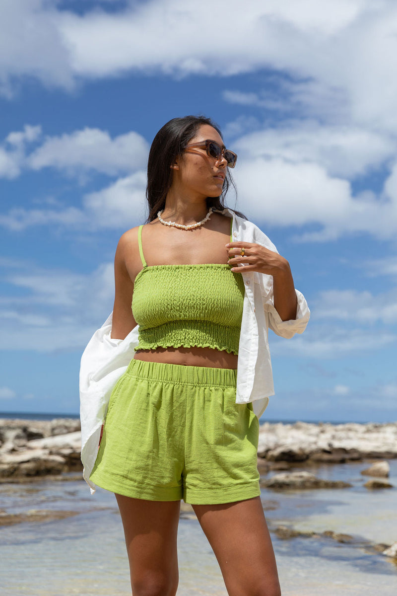 The YIREH A La Mode Button-Up in Cloud is a linen, slightly oversized, long-sleeve button-up featuring mother-of-pearl shell buttons.  - on one shoulder w/ Parakeet Millie Short & Rumi Bandeau